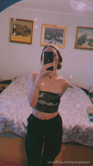 Woman in camo crop top and black pants takes mirror selfie in bedroom.