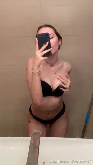 Woman in black lingerie posing in bathroom mirror selfie.