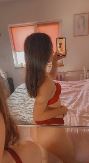 Woman in red lingerie taking mirror selfie in bedroom.