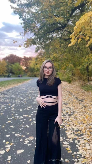 Woman in black crop top and pants standing on leafy path outdoors.