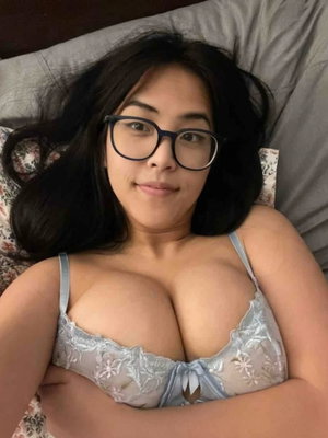 Woman with dark hair and glasses lying in bed, wearing light blue lace lingerie.