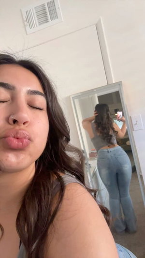 Curvy brunette in gray top and jeans, mirror selfie.
