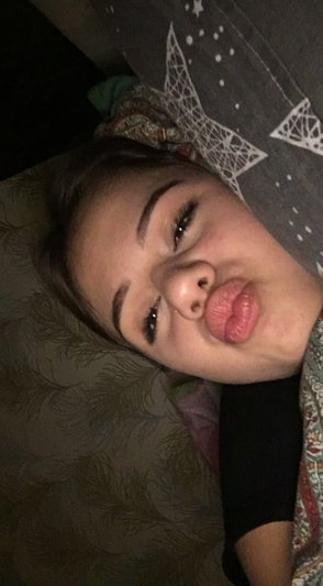 Woman with dark hair lying on patterned bedding, making a playful face with lips puckered.