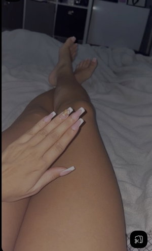 Woman's legs on bed with hand resting on thigh.