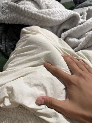 Hand resting on white fabric over a leg in bed.