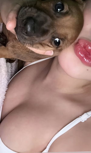 Buxom woman with glossy lips holding puppy, white lingerie top.
