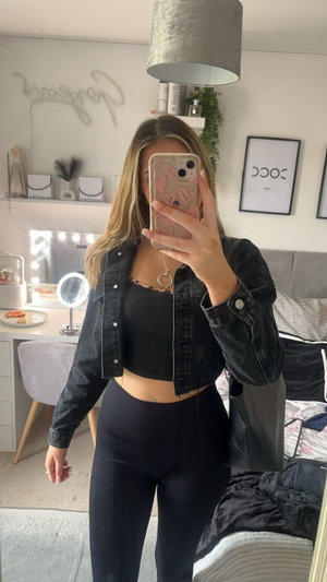 Blonde woman in open black jacket, lace top, leggings, bedroom selfie.