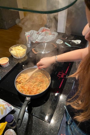 Woman with long hair stirring pasta in kitchen.