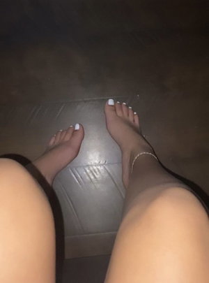 Woman's bare feet with white nail polish and anklet, wearing black sheer stockings, standing on