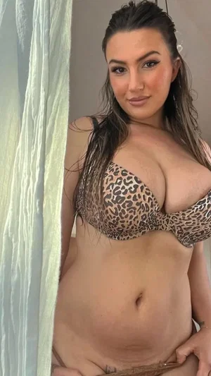 Curvy woman with dark hair wearing leopard print bra indoors.