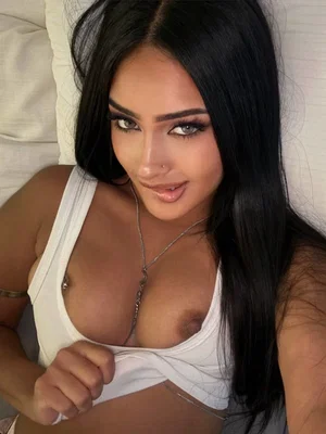 Woman with long black hair in white top on bed.