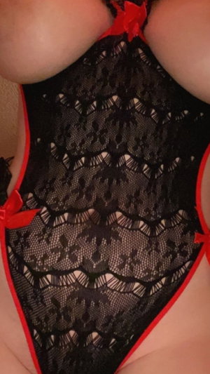 Woman in black lace lingerie with red trim, close-up of chest and torso.