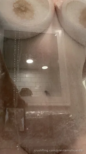 Reflection of person in bathroom mirror, wearing dark top, tiled walls, shower curtain visible.