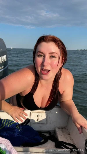 Woman with wet red hair in black bikini top on a boat, smiling at camera.