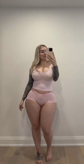 Blonde woman in pink tank top and underwear, full-body mirror selfie, tattoos on arms, indoor