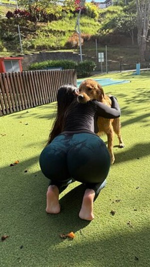 Woman in black top and leggings kneeling outdoors hugging a dog.
