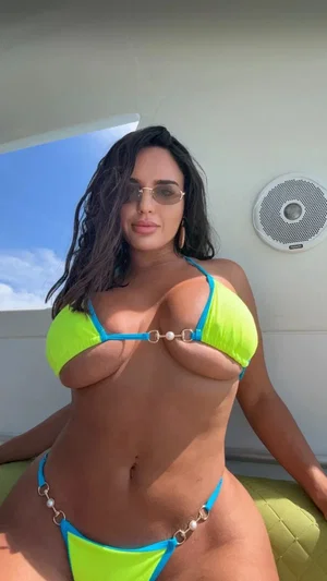 Woman in neon green and blue bikini posing on a boat, wearing sunglasses.