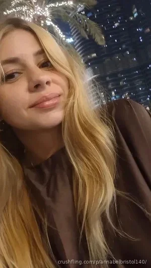 Blonde woman in brown top, indoor setting with city lights and palm fronds in background.