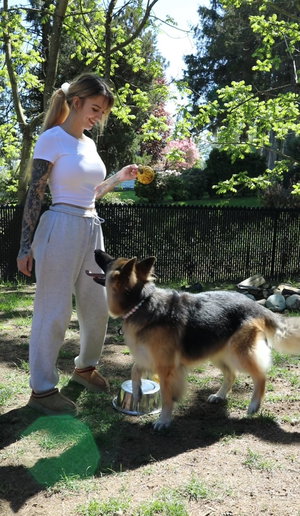 Woman in white tee and gray sweats with dog outdoors.