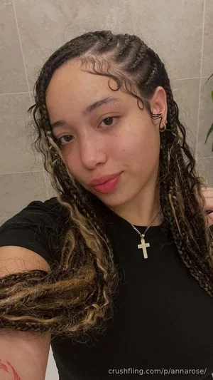 Woman with braided hair wearing black top, indoors, close-up selfie.