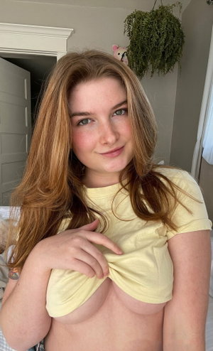 Woman with red hair lifts yellow shirt in bedroom.