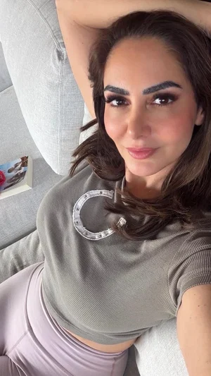 Woman with dark hair in a gray crop top and lavender leggings, lying on a couch.