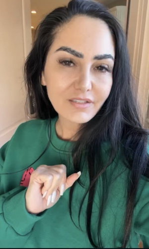 Woman with long dark hair wearing green sweatshirt indoors, looking at camera.