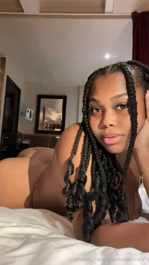 Woman with braided hair lying on bed, topless, in a bedroom setting.