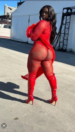 Woman in red lace bodysuit and thigh-high boots posing outdoors near white tent.