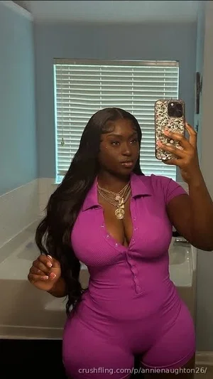 Woman in purple ribbed jumpsuit takes mirror selfie in bathroom.