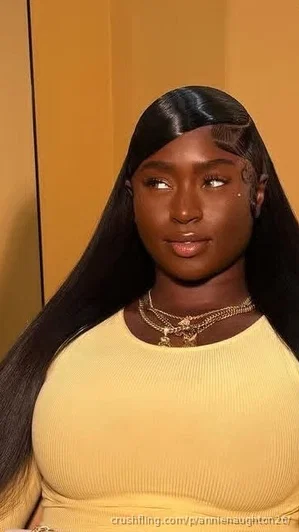 Woman with long black hair wearing yellow ribbed top, gold necklaces, indoors.