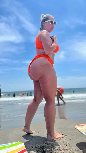 Woman in orange bikini standing on beach, back view, sunny day.