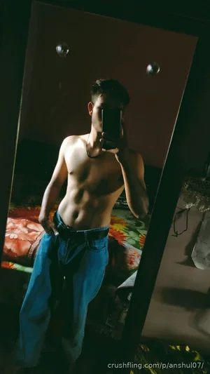 Shirtless man with defined abs wearing jeans, taking mirror selfie in dimly lit room.