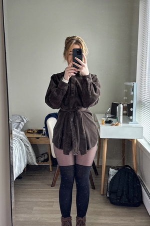 Woman in brown corduroy mini dress, black thigh-highs, boots, bedroom mirror selfie.