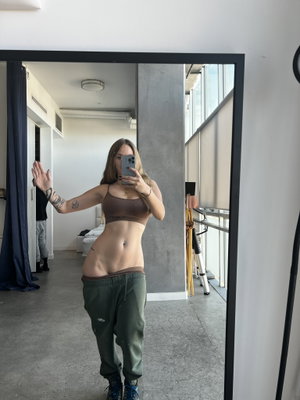 Fit woman with tattoos taking mirror selfie indoors in crop top.