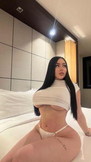 Curvy woman in white crop top and thong on bed.