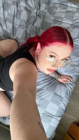 Woman with red hair and glasses in black top lying on checkered bedspread.