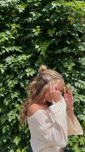 Woman with blonde hair in a bun wearing off-shoulder white sweater, standing outdoors in front of