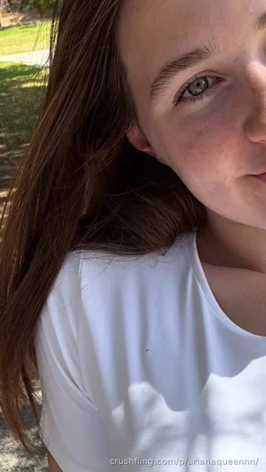 Woman with long brown hair and green eyes wearing white t-shirt outdoors.