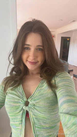 Woman with brown hair in a green striped top, taking a selfie indoors.