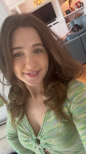 Woman with long brown hair in a green striped top, smiling in a living room.