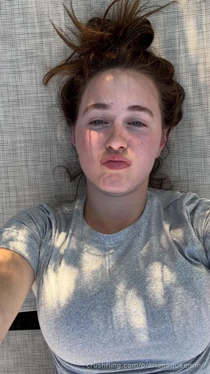 Woman with messy hair lying on textured surface, wearing gray t-shirt, outdoor lighting.