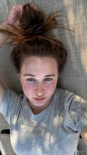 Woman with brown hair in bun, wearing gray t-shirt, lying on textured surface.