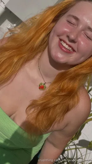 Woman with long red hair in green top, smiling outdoors.