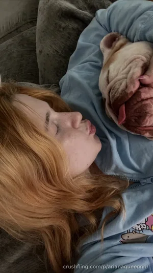 Woman with red hair sleeping next to a dog, wearing a blue hoodie, indoor setting.