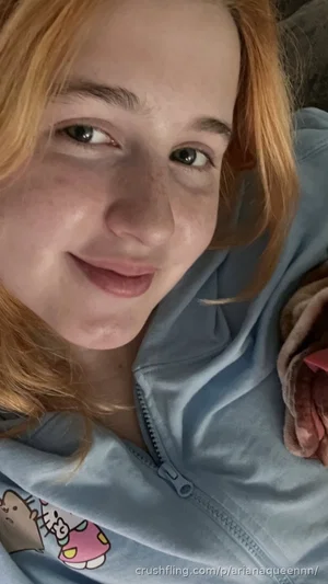 Woman with red hair in light blue zip-up hoodie, smiling in close-up selfie.