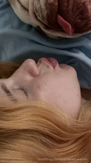 Woman with red hair lying down, face close to a dog's face, both resting on blue fabric.