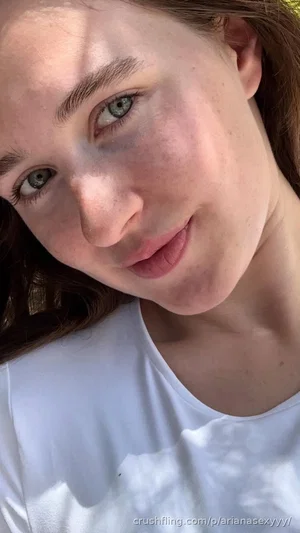 Woman with freckles and green eyes wearing white top, outdoor selfie.