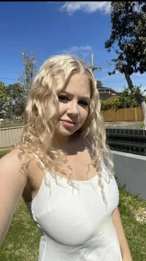 Blonde woman in white spaghetti strap top outdoors.