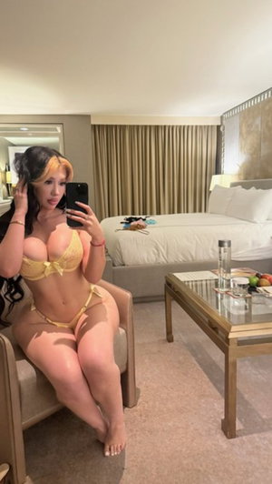 Woman in yellow lingerie taking selfie in hotel bedroom.